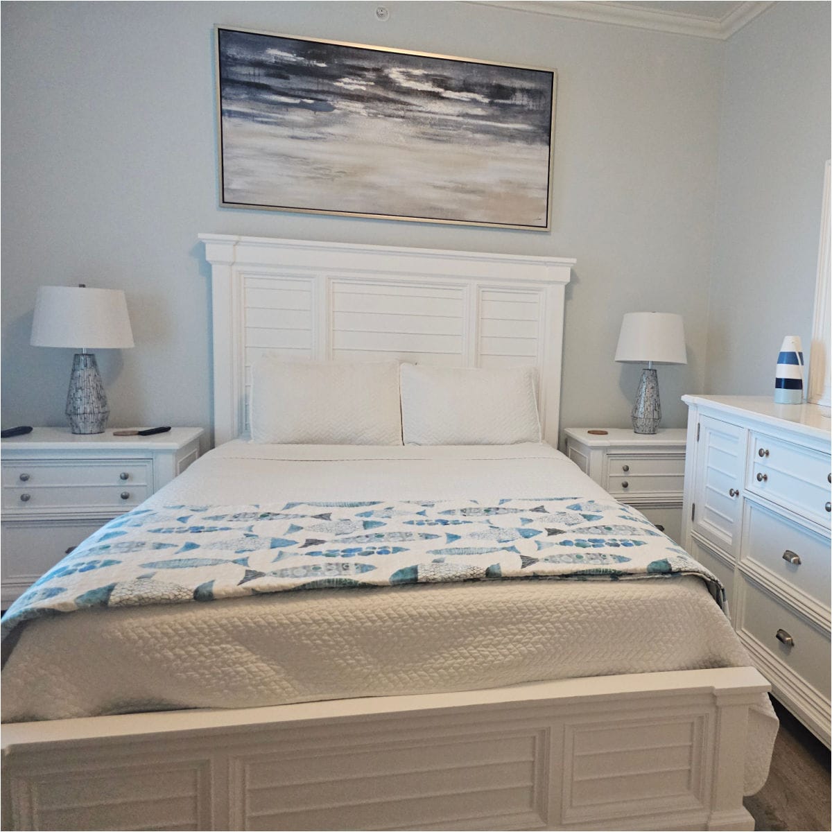 Bedroom with white headboard on the bed, fish blanket at the end of the bed, white dresser and nightstands next to the bed