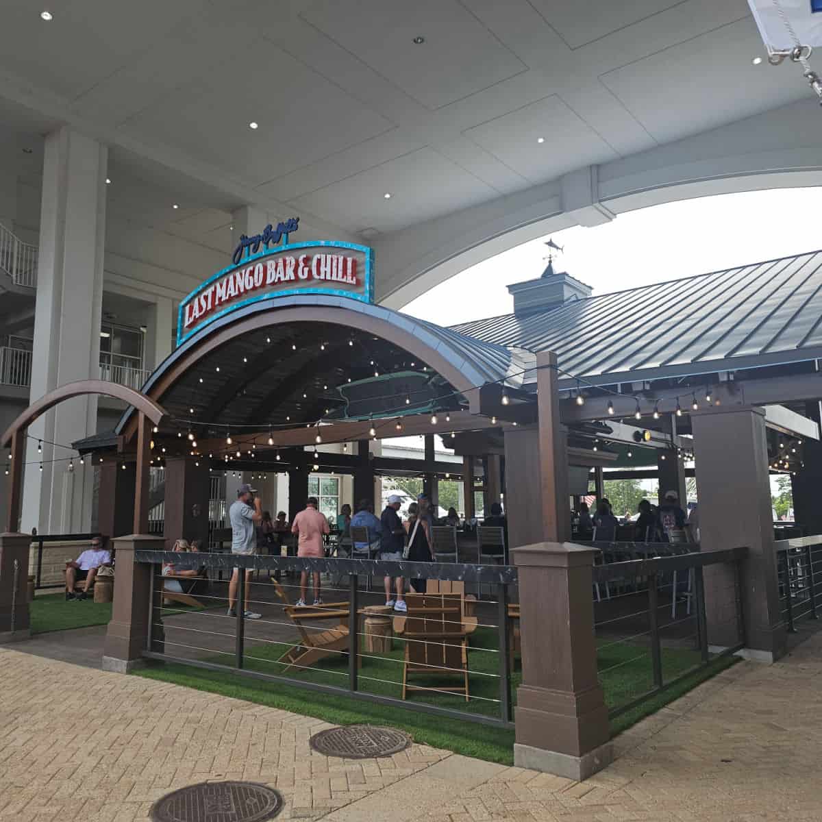 Jimmy Buffett's Last Mango Bar & Chill sign over an outdoor boat with a covered roof, Adirondack Chairs along with bar seating.