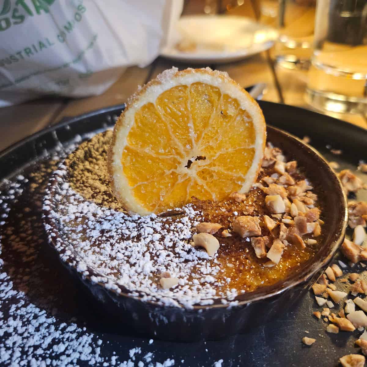 candied orange in a creme brule dish surrounded by hazelnuts on a dark plate