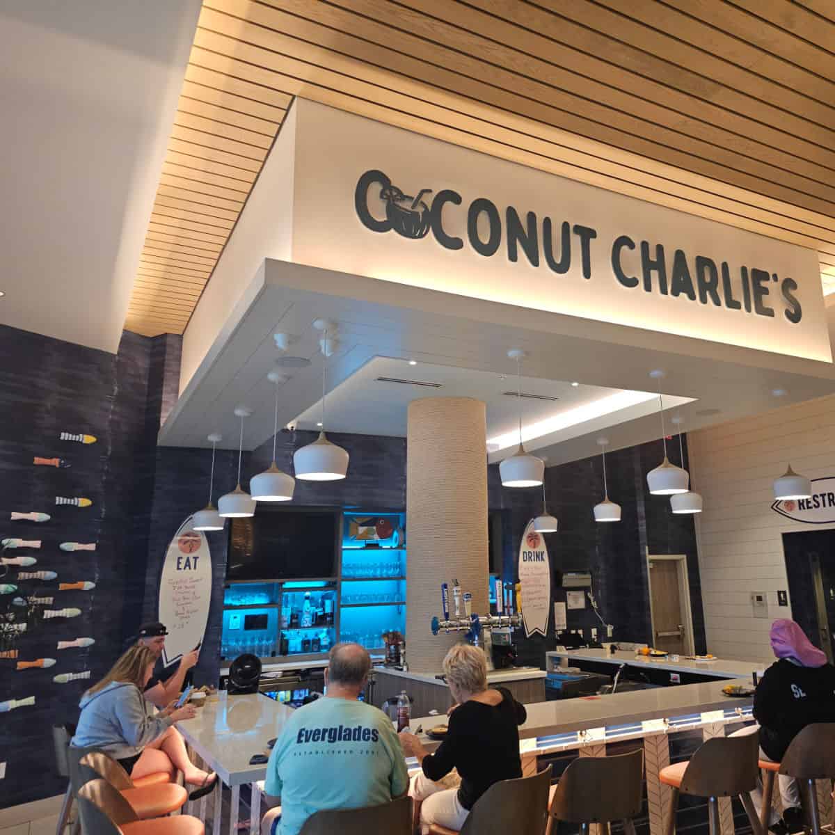 Coconut Charlies printed on the top of a bar cover with people sitting around the square bar