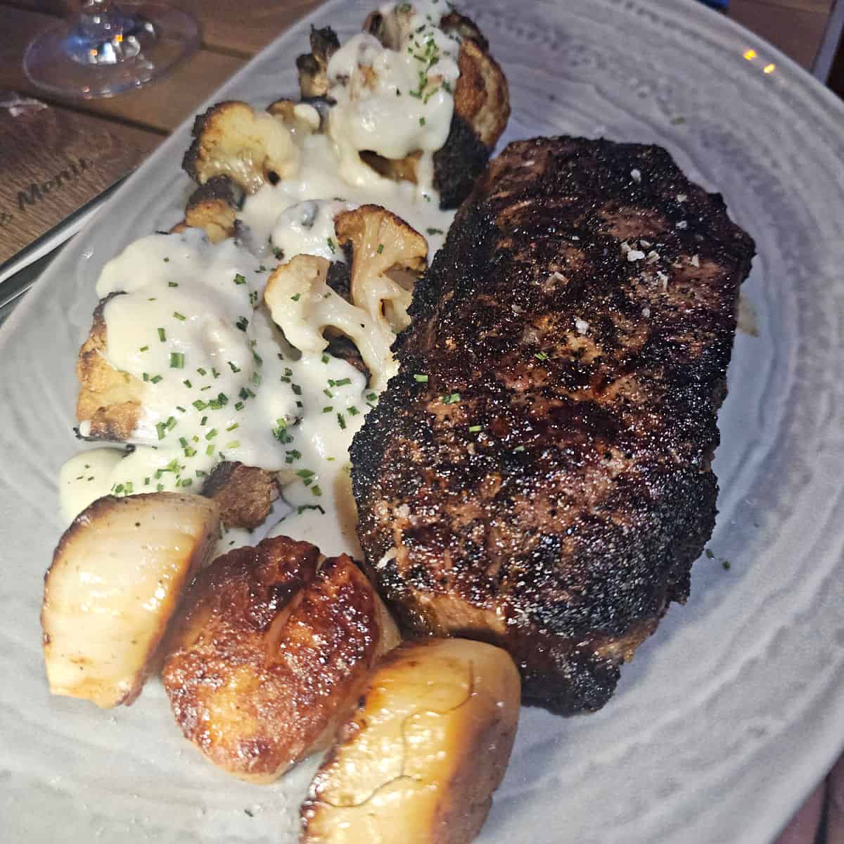coffee rubbed ny strip steak on a white plate with scallops and cauliflower covered in sauce