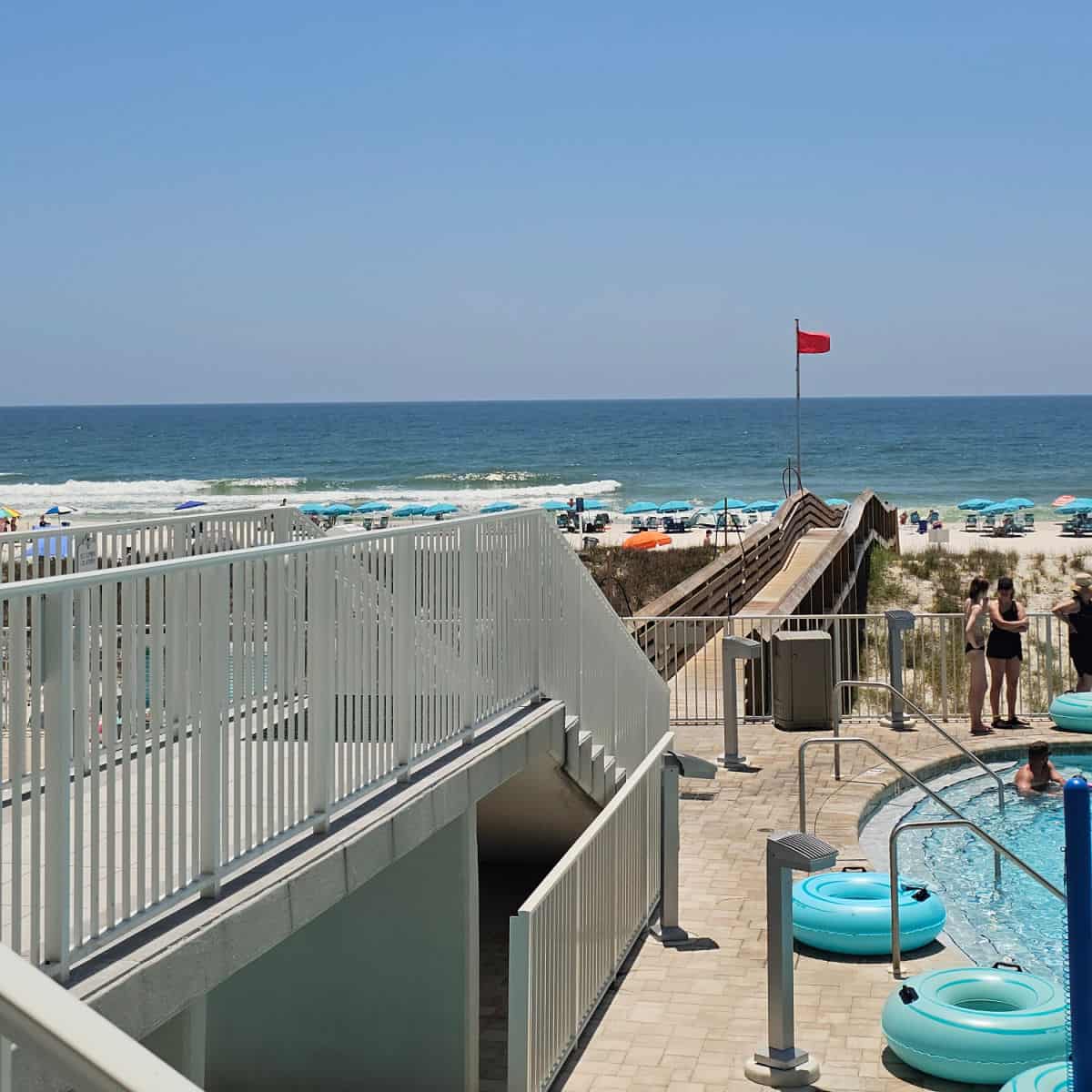 walkway over the sand dunes to the beach with umbrellas along the beach and Gulf waters