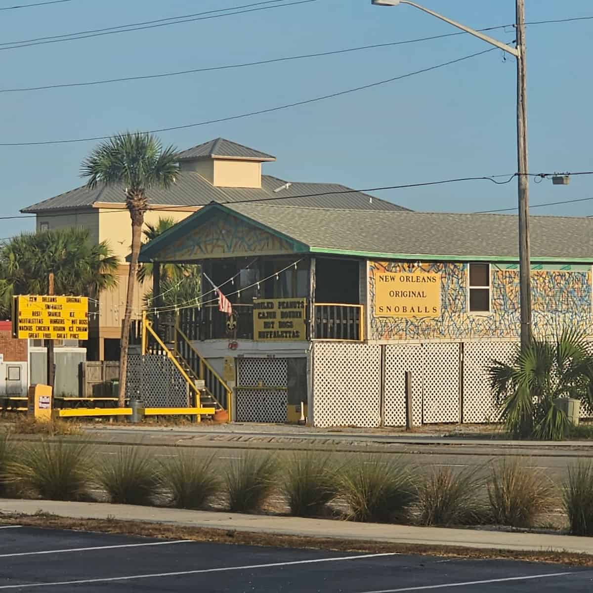 Exterior of New Orleans Original Snoballs with sign on the side of the building with fun paint around the building, white lattice work around the base of the building.