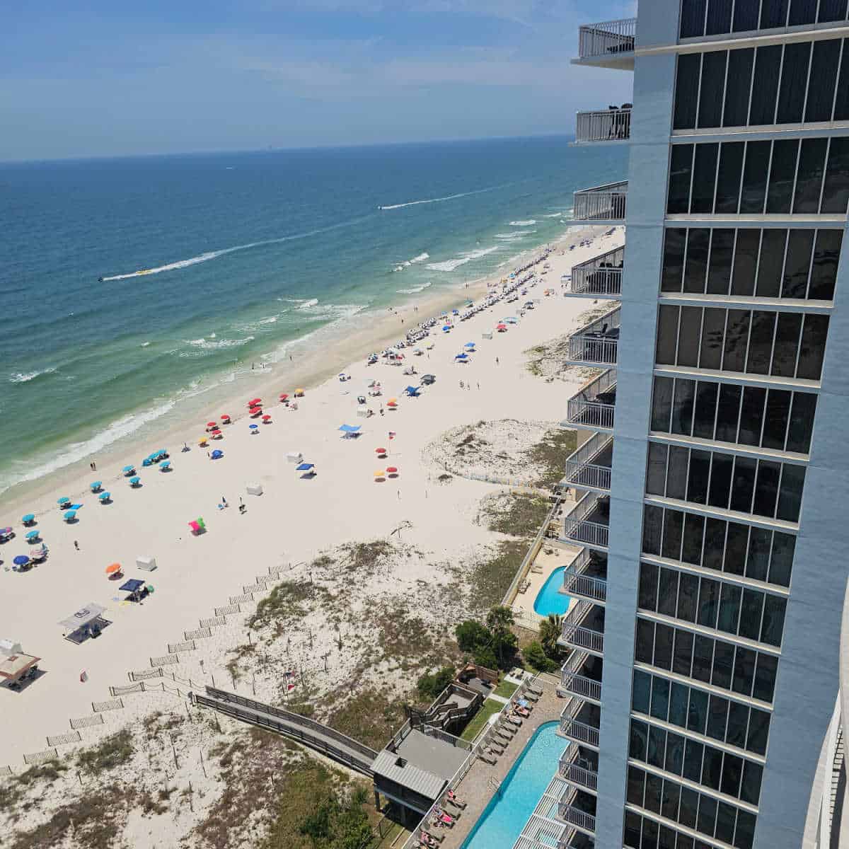 looking out towards the Gulf Shores beach from a high floor with colorful umbrellas along the beach, pools next to condo buildings