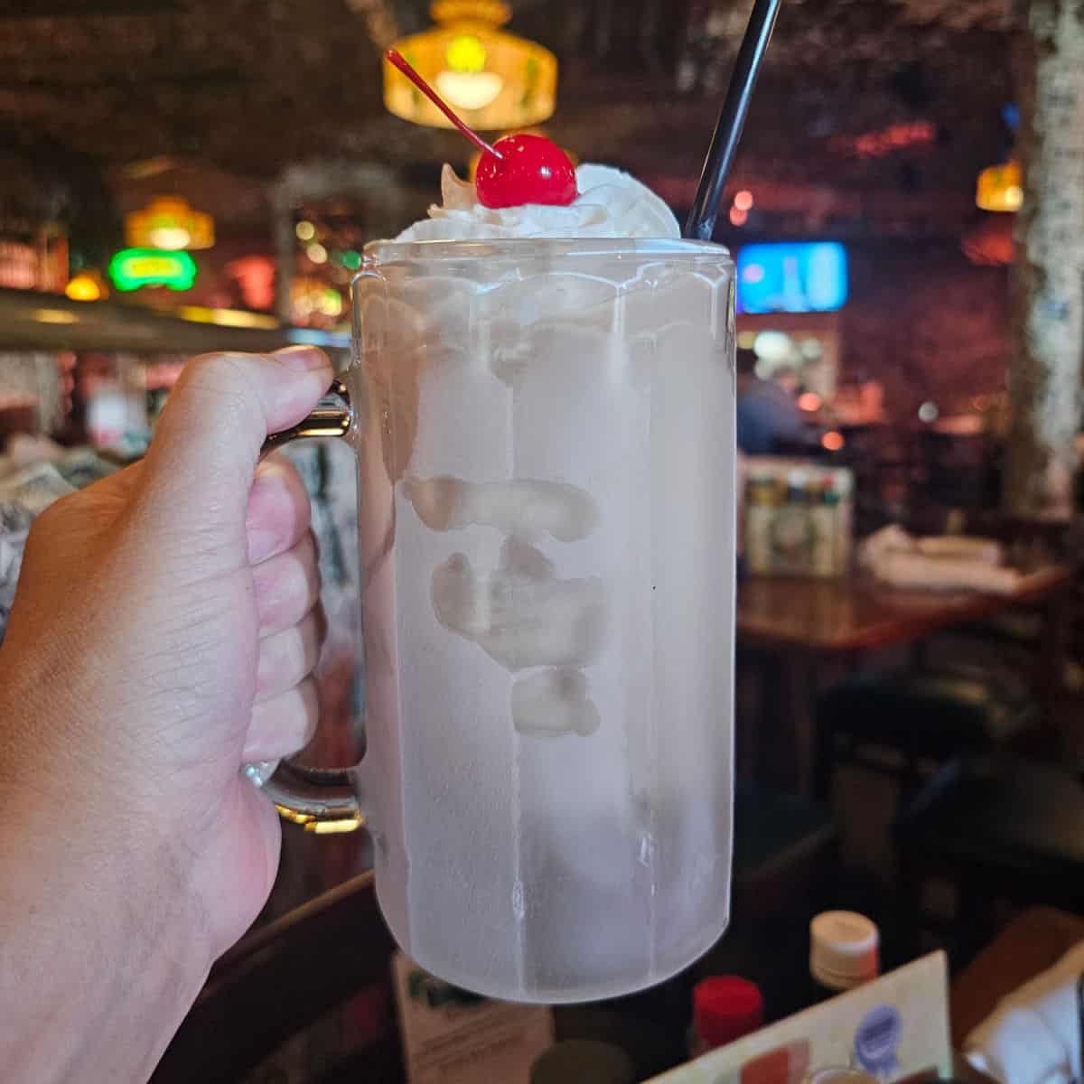 Hand holding a frozen irish coffee in a mug topped with whipped cream and a cherry