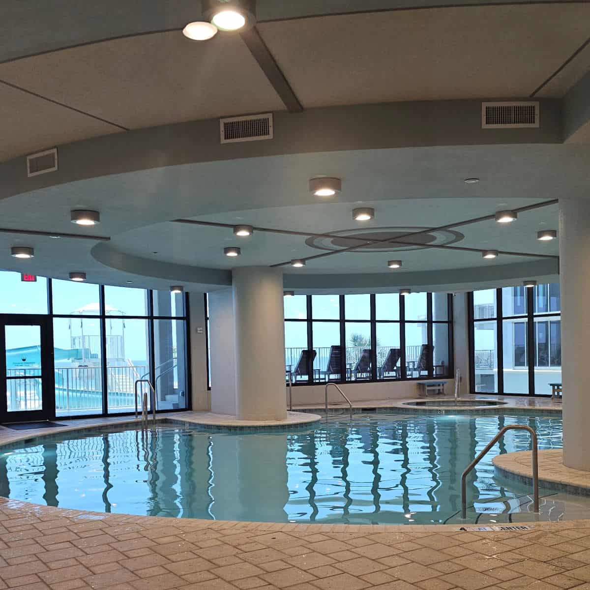 indoor pool and hot tub with glass windows looking out towards the beach