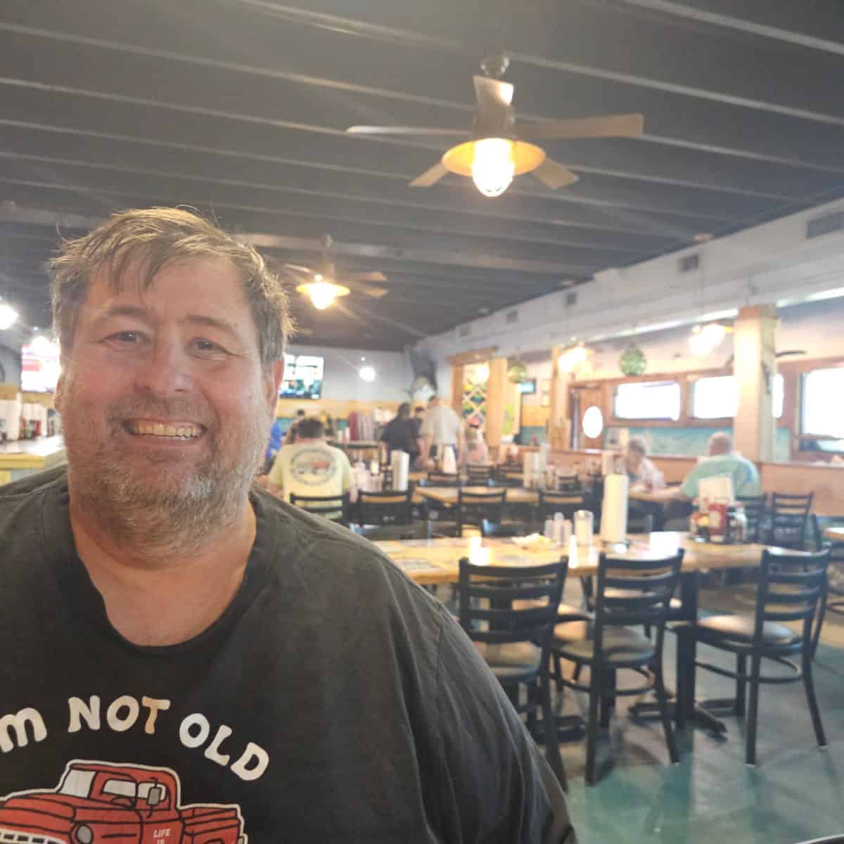 John smiling in Shipwrecked Raw Bar with tables and chairs behind him