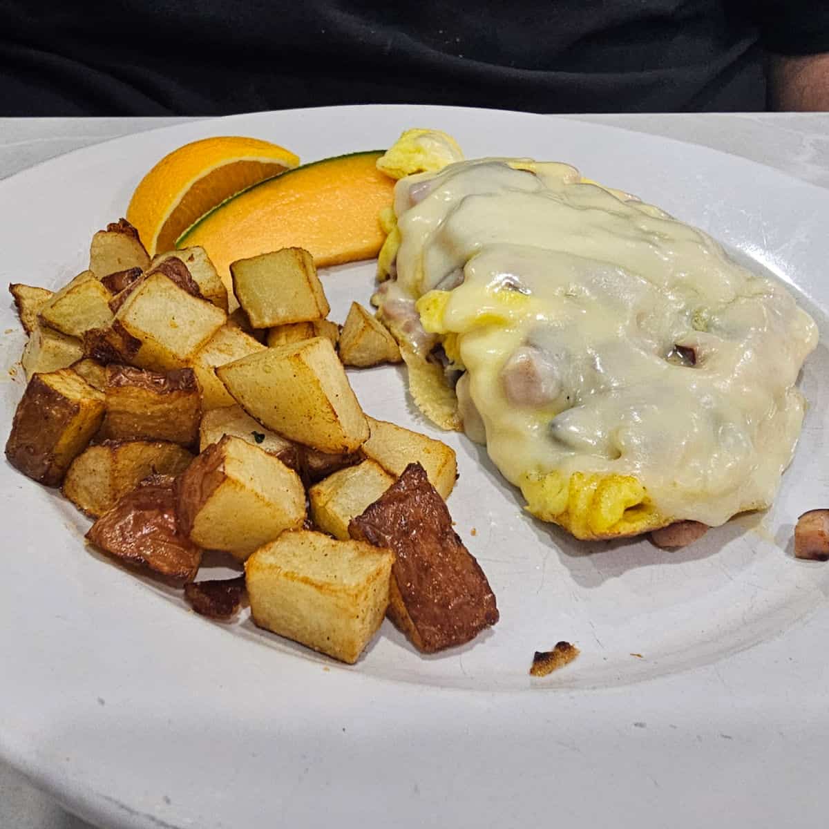 cheese covered omelet on a white plate with potatoes and slices of cantoloupe