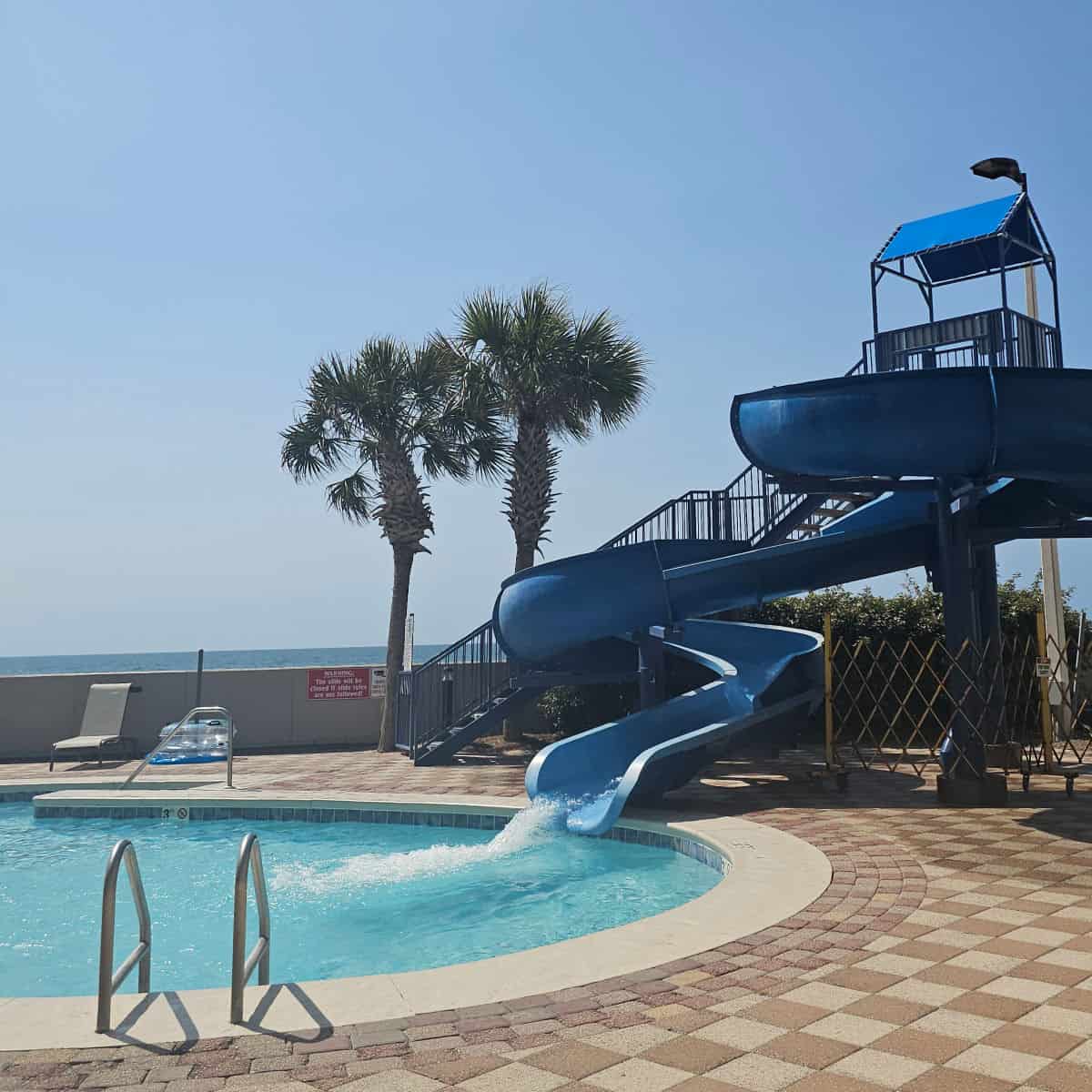 Blue waterslide leading down into a pool, palm trees next to the waterslide