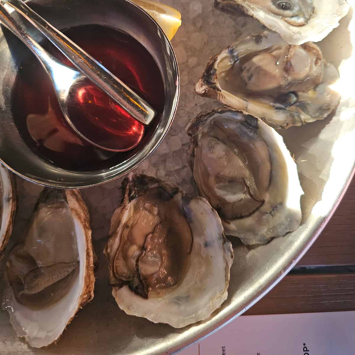 oysters in a silver dish on ice with a bowl of sauce in the middle
