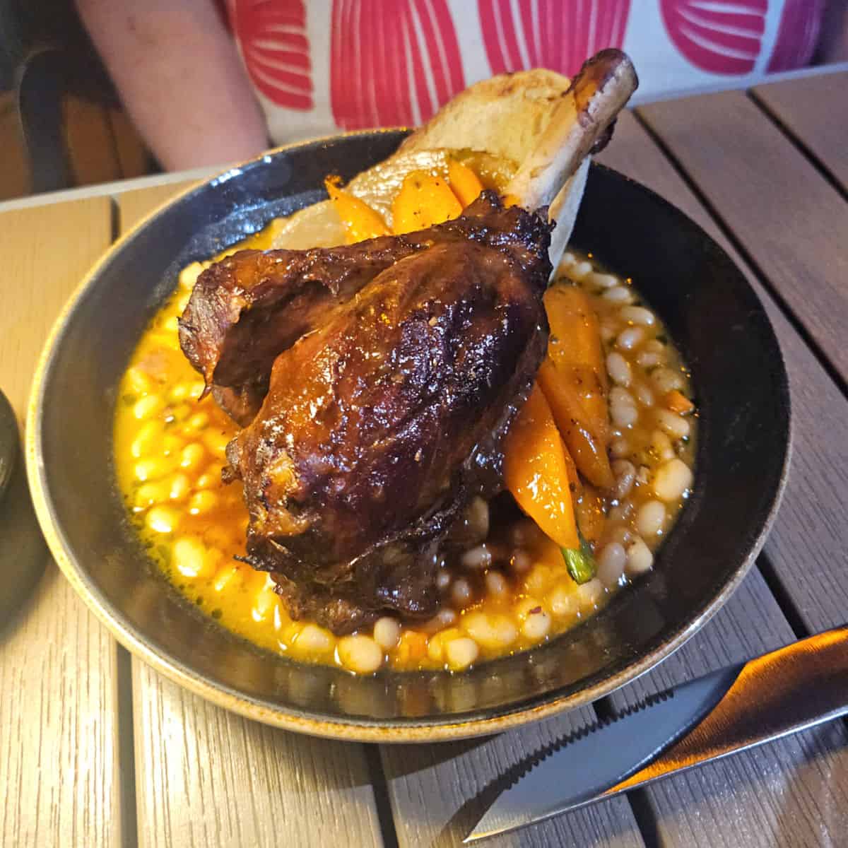 circle plate with a leg of lamb over beans on a table