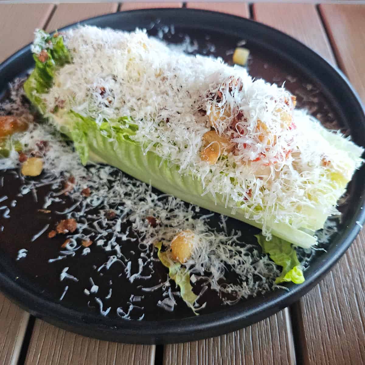 wedge salad covered in cheese on a dark plate
