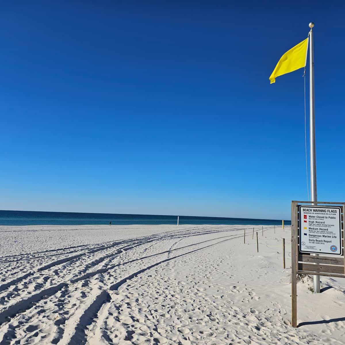 white sand beach with yellow beach flag, beach warning flag informational sign, Gulf waters and blue skies