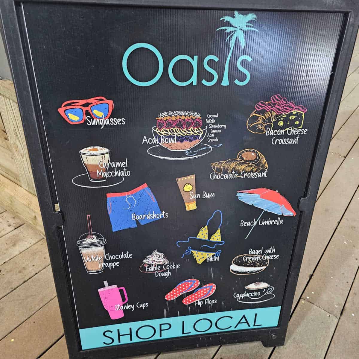 Oasis shop local sign with drawings of sunglasses, acai bowl, bacon cheese croissant, sun bum, boardshoarts, umbrellas, stanley cups, flip flops, and coffee drinks