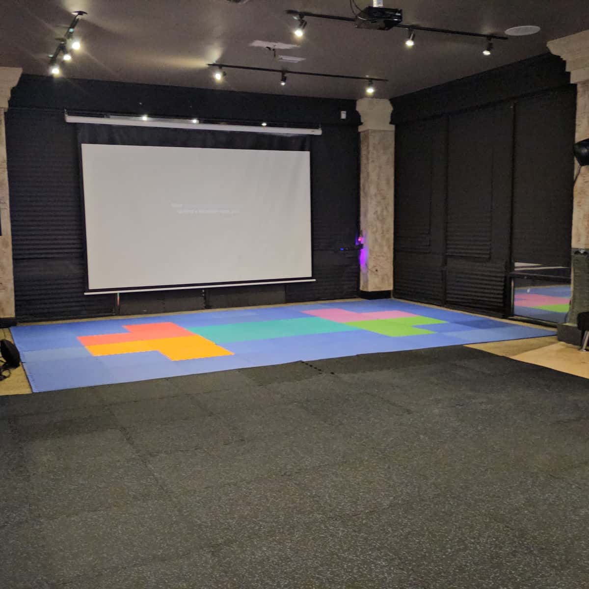 open area with a screen on the wall and colorful mat on the floor