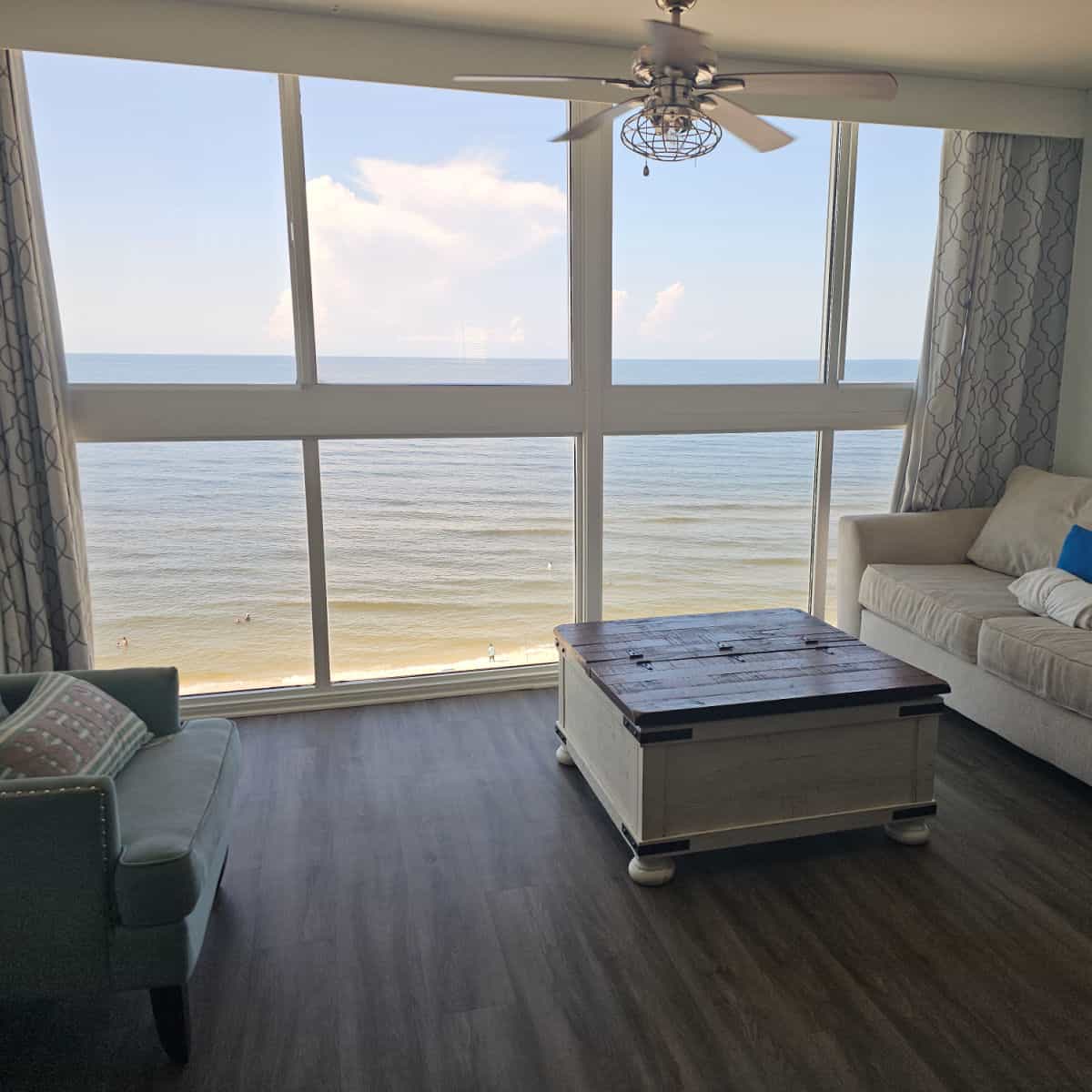 looking out a large glass window to the Gulf water, couch on one side with a table, chair on the other side of the room