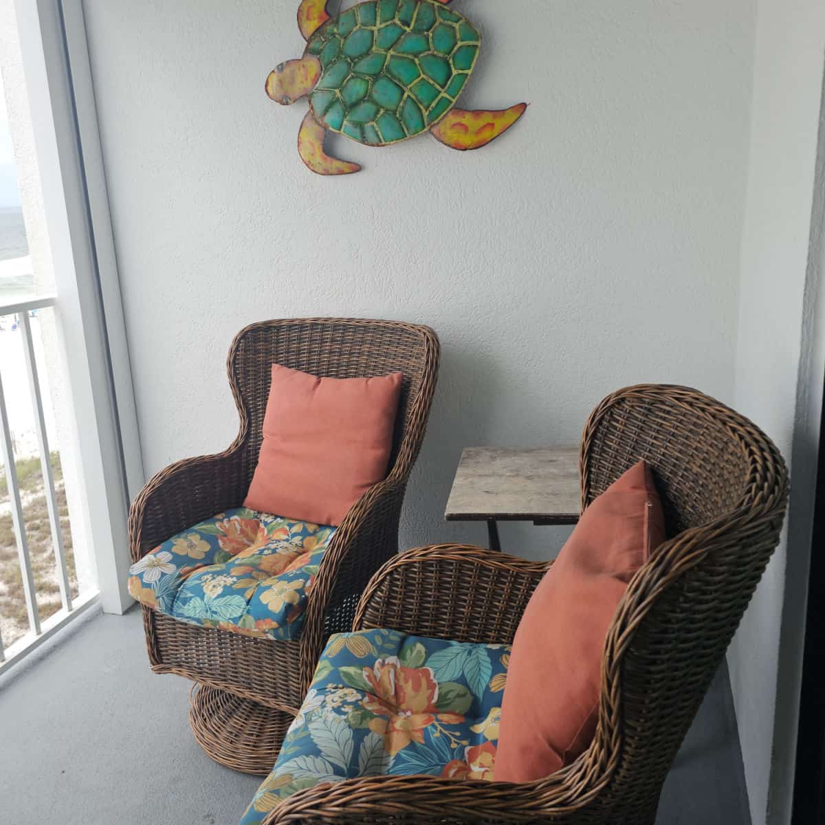 balcony with two brown chairs with floral and orange cushions, turtle sculpture on the wall