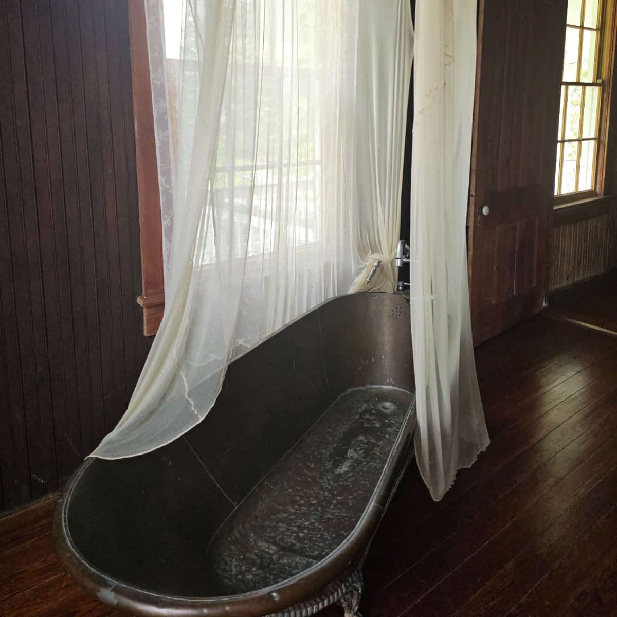 metal bathtub with sheer gauze around it in a room with wooden walls