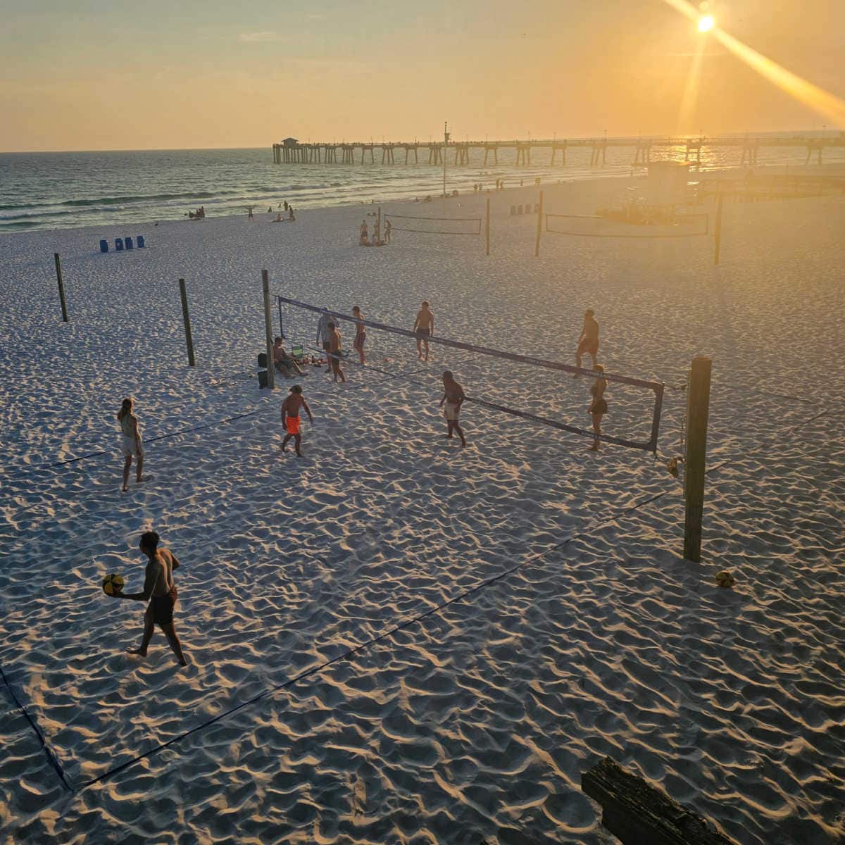 beach volley ball game happening below on the beach with the pier in the background at sunset