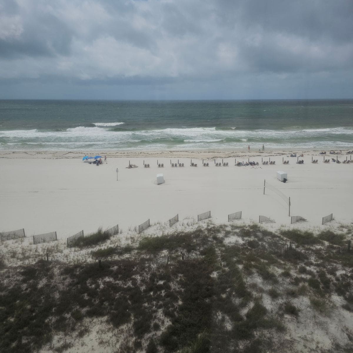 looking out to the beach on a cloudy stormy day with beach chairs and people alnog the water edge