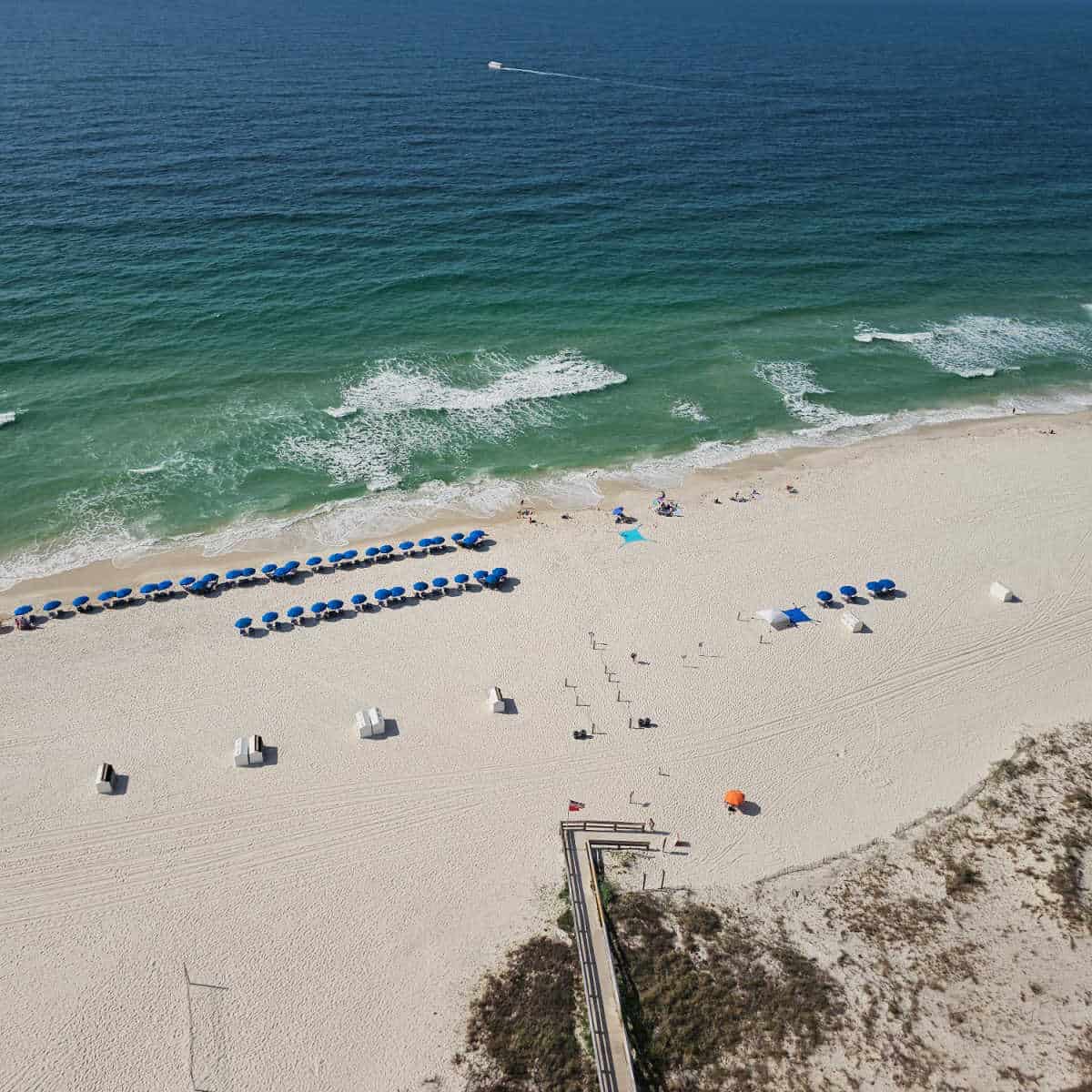 looking down on a white sand beach with elevated walkway over the sand dunes, blue umbrellas lined up along the shoreline