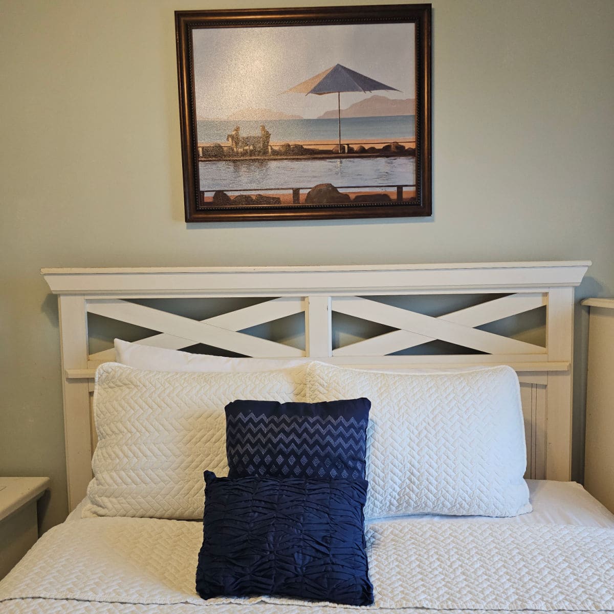 Bedroom with wooden headboard on the bed with white and blue pillows, coastal art on the wall