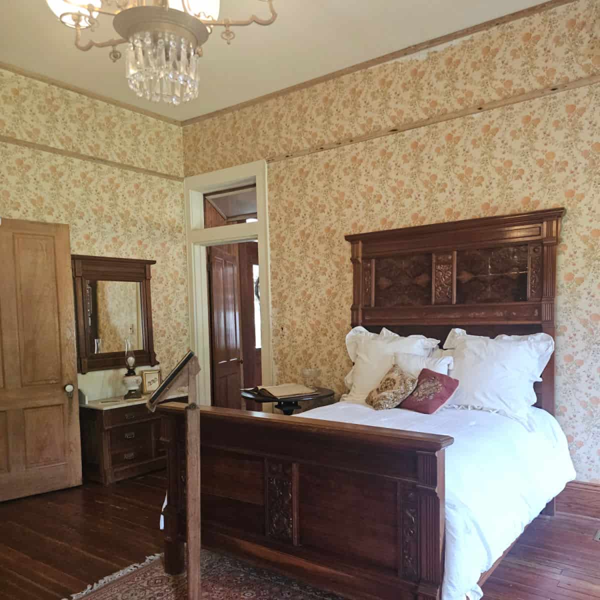 bedroom with floral brown and orange wallpaper, with a bed that has a large wooden headboard and footboard, mirror and cabinet along the far wall