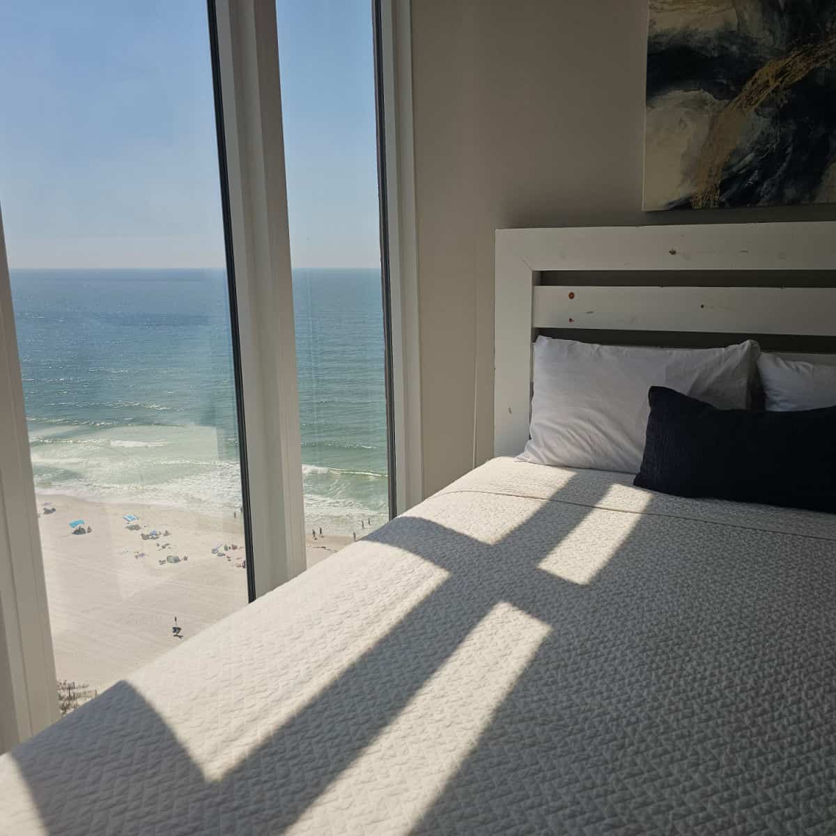 Window overlooking the beach and Gulf water with a bed with white linens and pillows