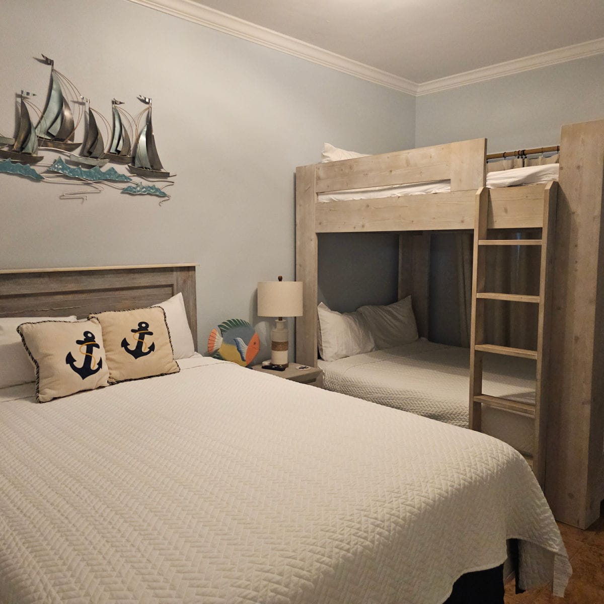 Bedroom with bed next to a wooden bunk bed with latter up the side, sailboat art on the blue walls