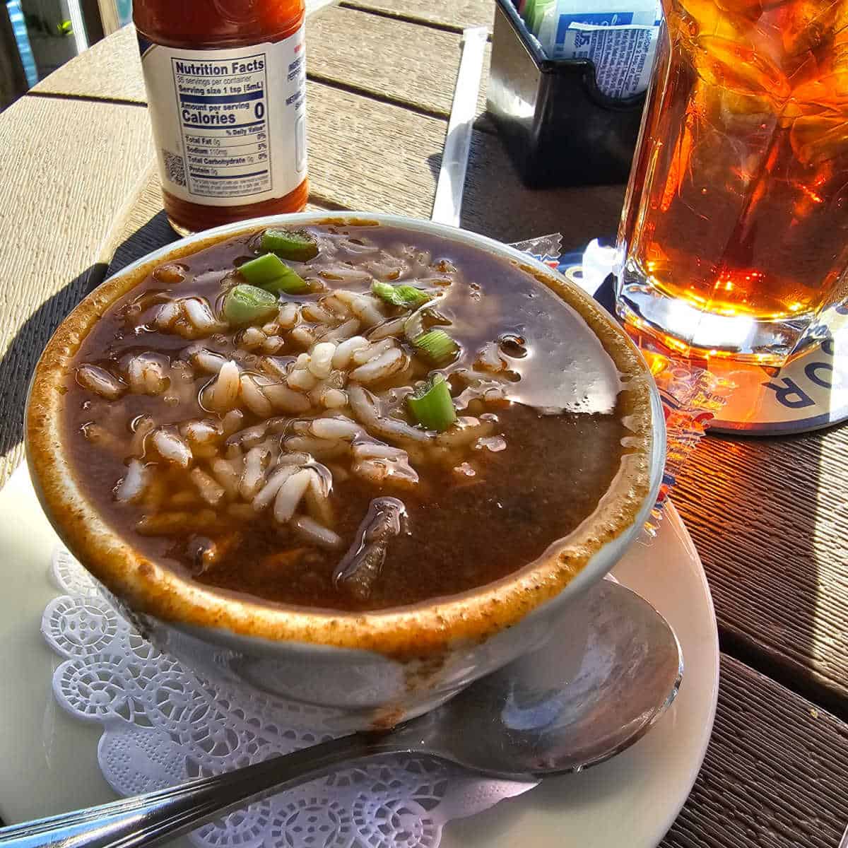 gumbo in a white bowl next to a glass of tea