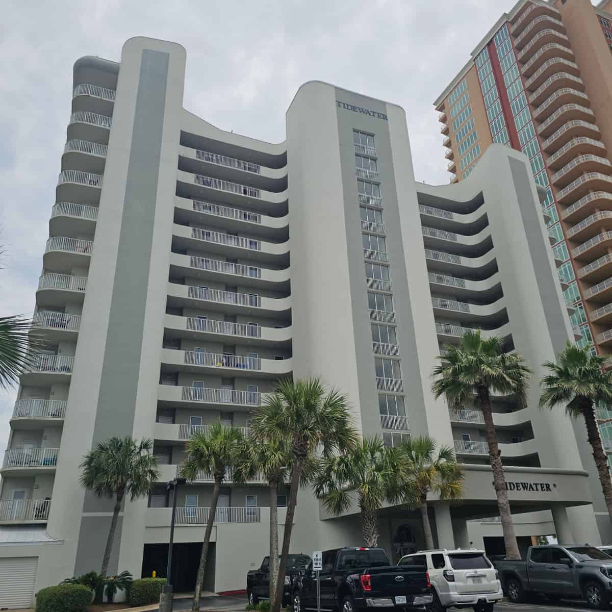 Tidewater printed on the top and bottom of the building, multi-story building with palm trees in the parking lot and cars near the entrance