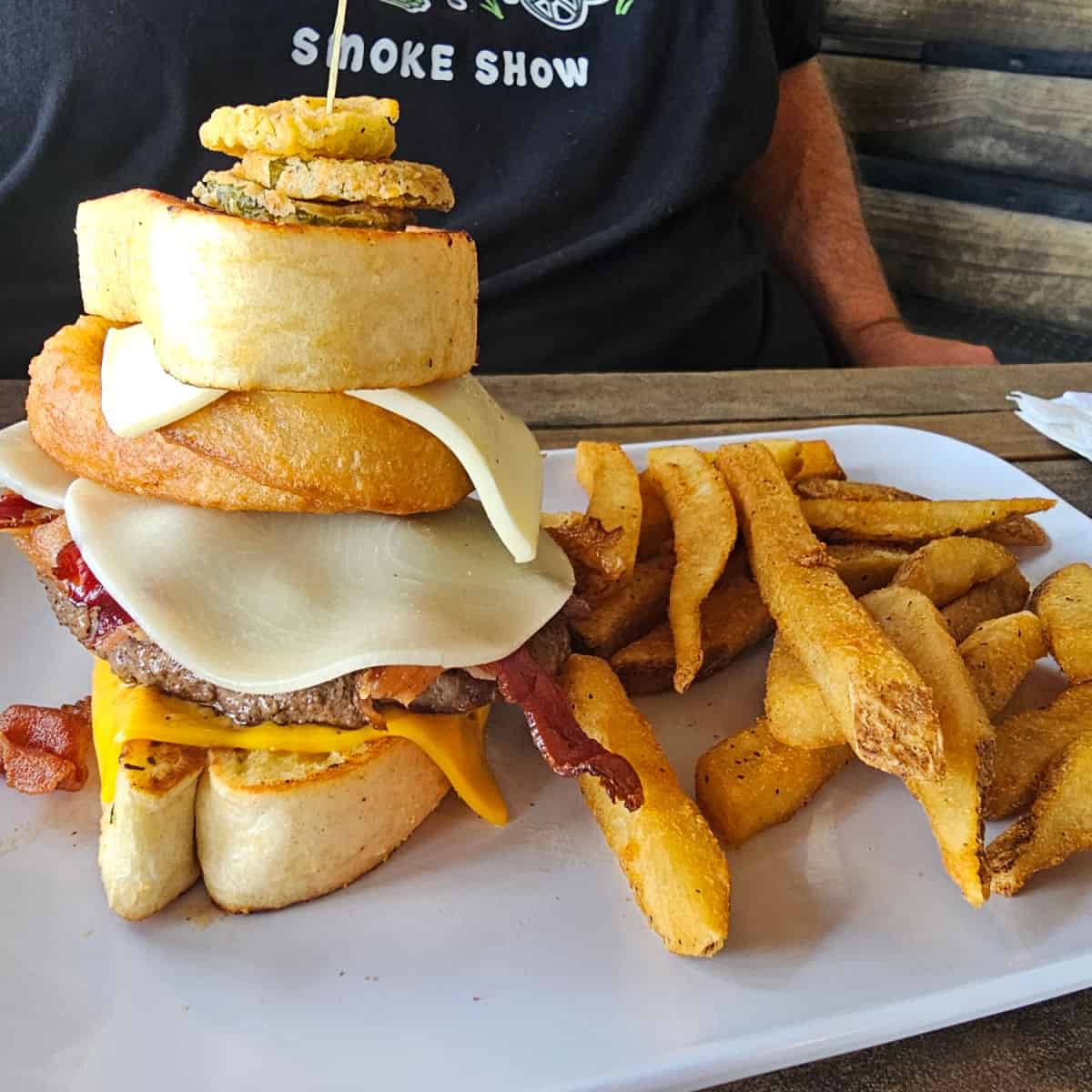 giant burger with onion rings and fried pickles on a white plate with fries
