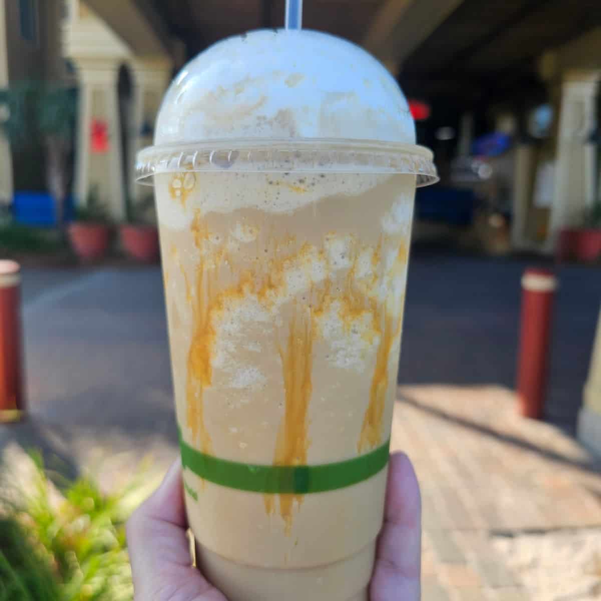 hand holding a caramel frappe with caramel dripping inside the cup