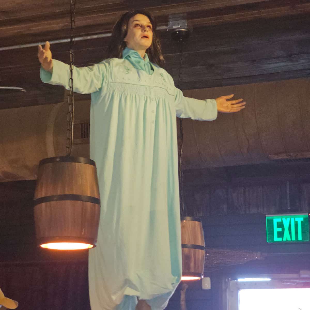 creepy large doll hanging from the ceiling near barrel lights and the exit sign
