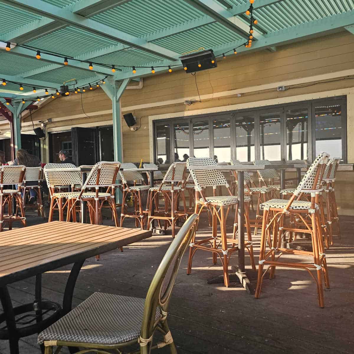 outdoor seating with tall tables with white and brown tall chairs in a row near a few lower tables