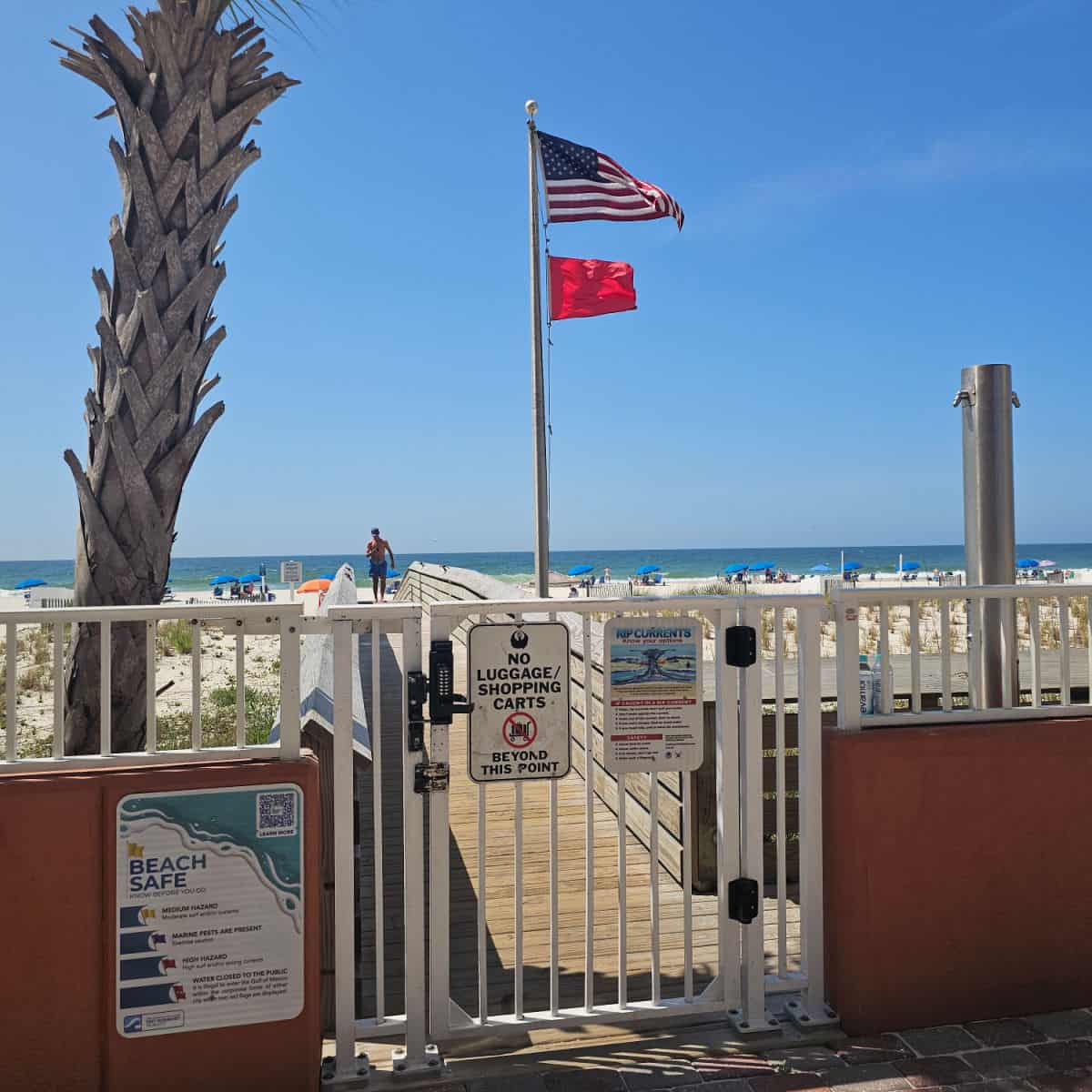 gate leading to a boardwalk to the beach, red flag and American flag flying