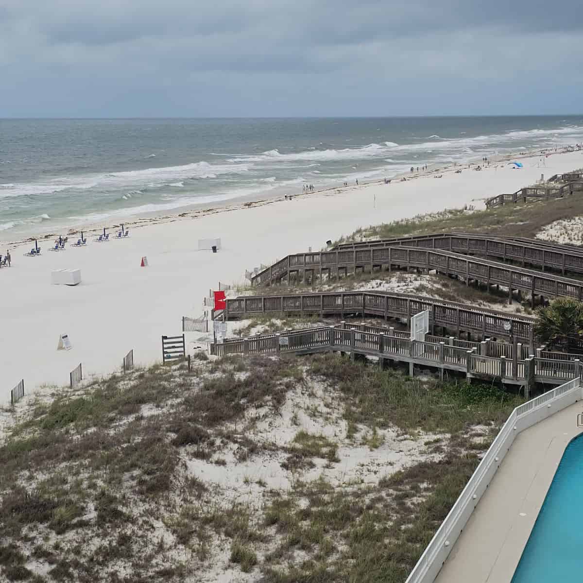 elevated boardwalk over the sand dunes leading to the beach with chairs along the beach, rough surf in the water