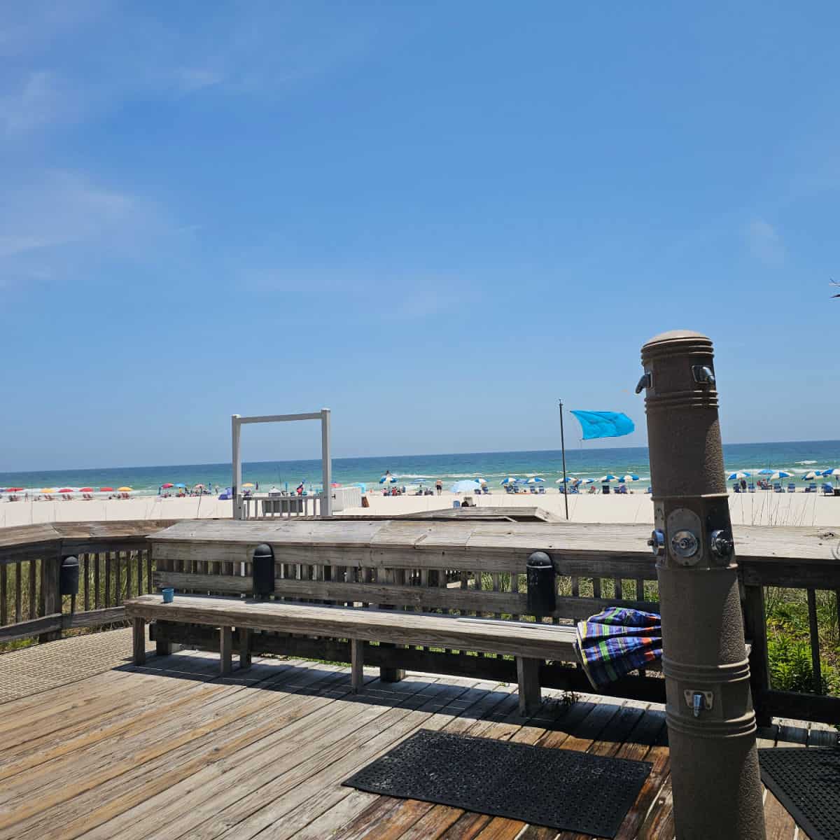 outdoor shower next to a wooden deck leading to the beach boardwalk with white sand and Gulf waters in the background