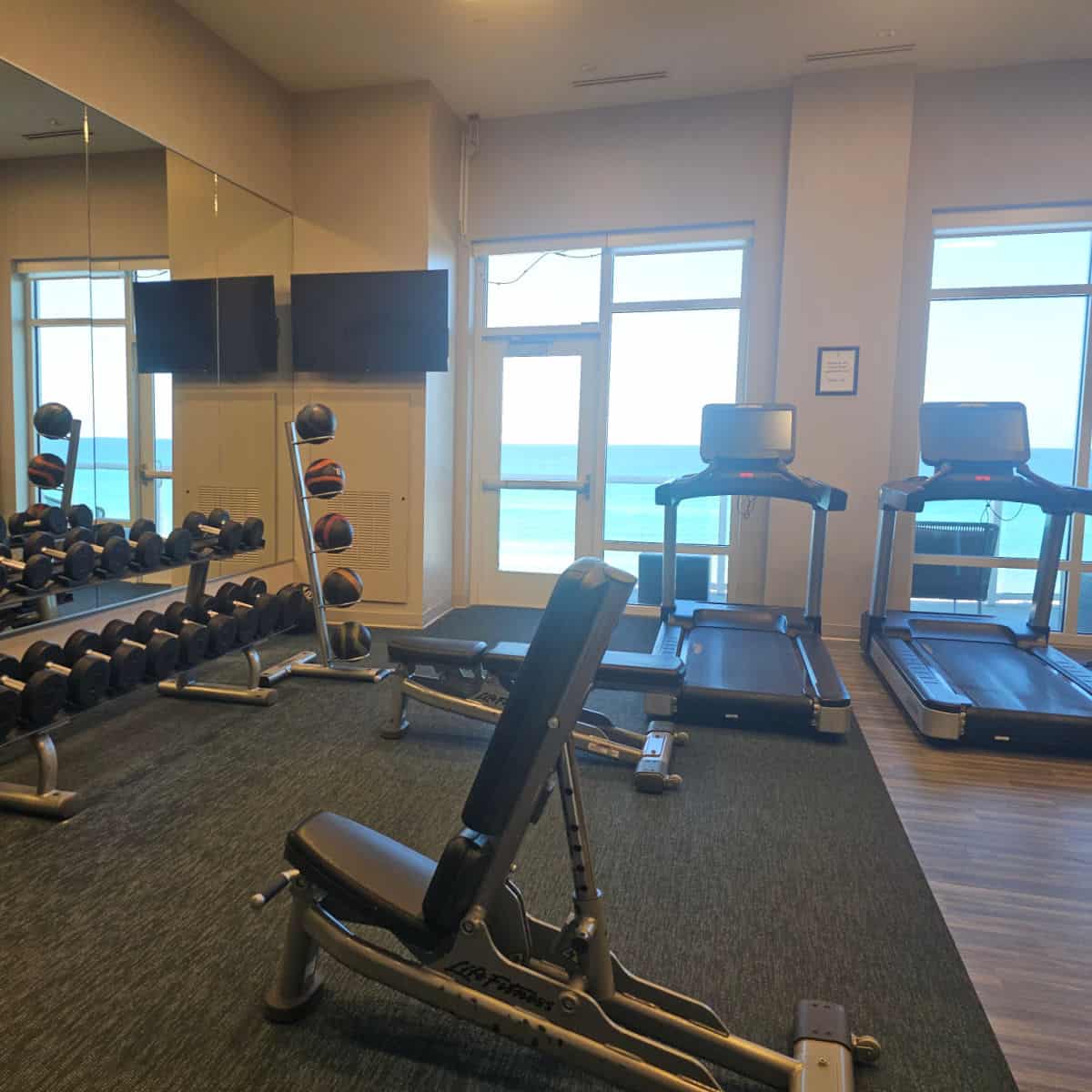 fitness center with treadmills looking towards the beach, free weights, and weight bench