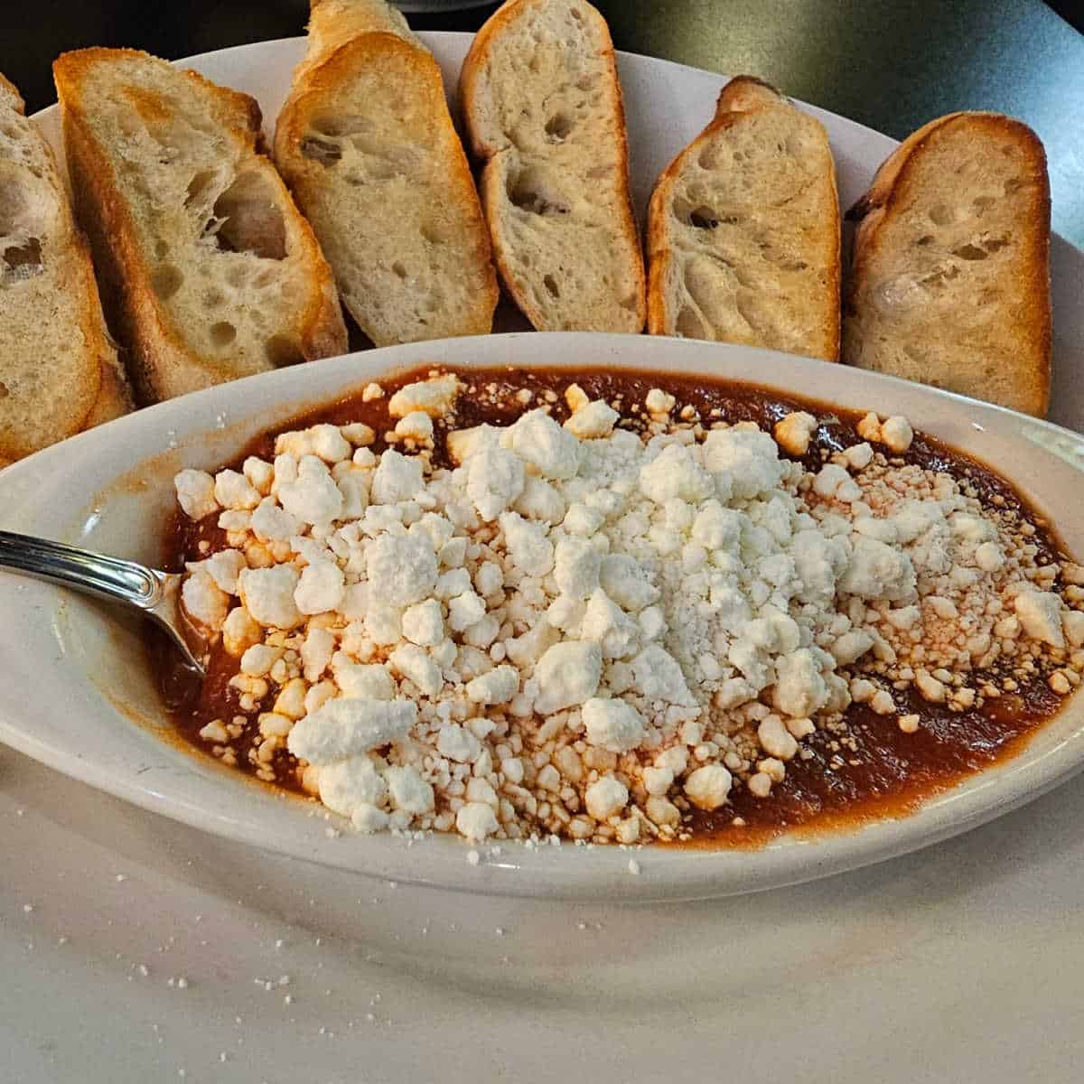 cheesey marinara dipping sauce in a bowl next to slices of tasted bread