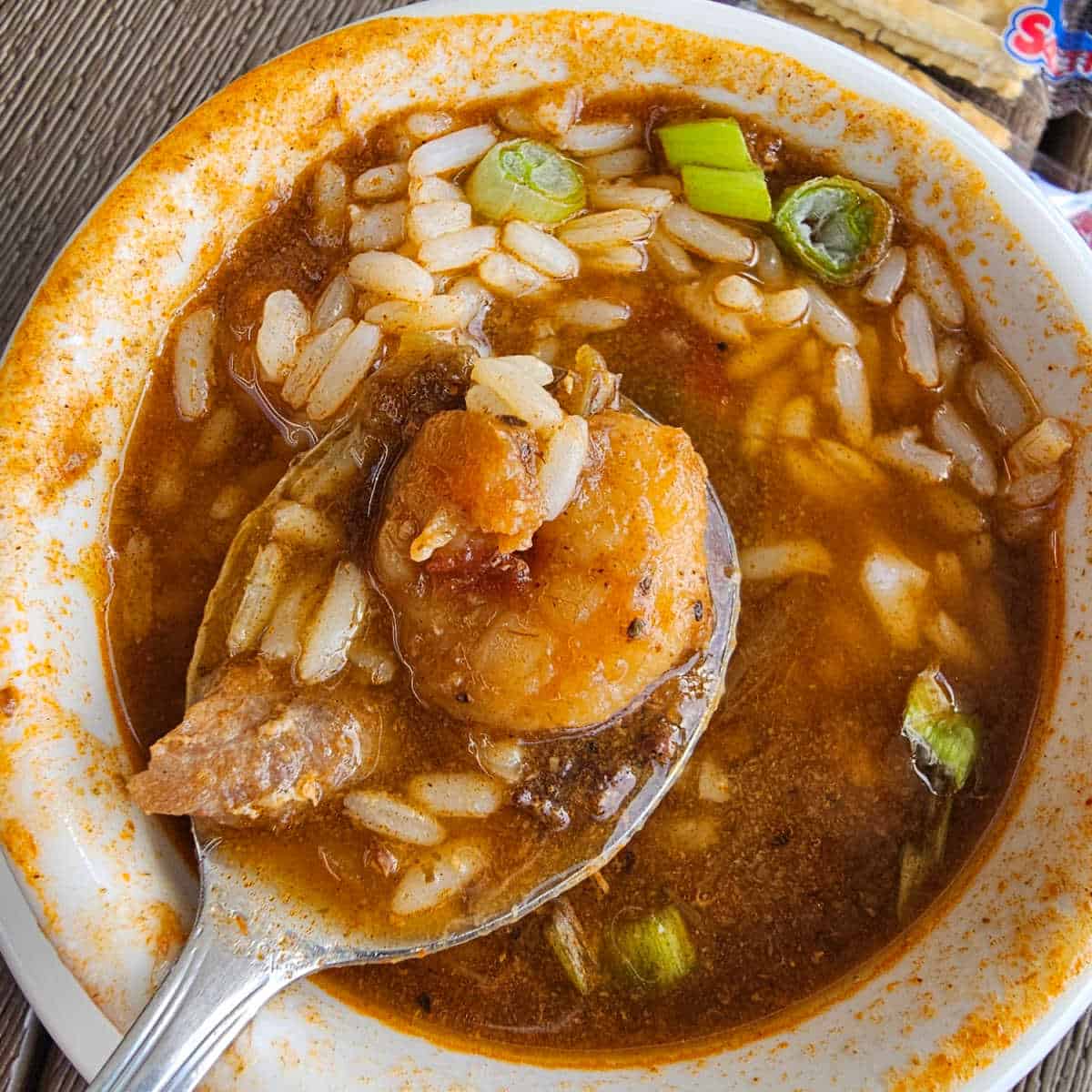 gumbo with a shrimp and rice on a spoon in a white bowl