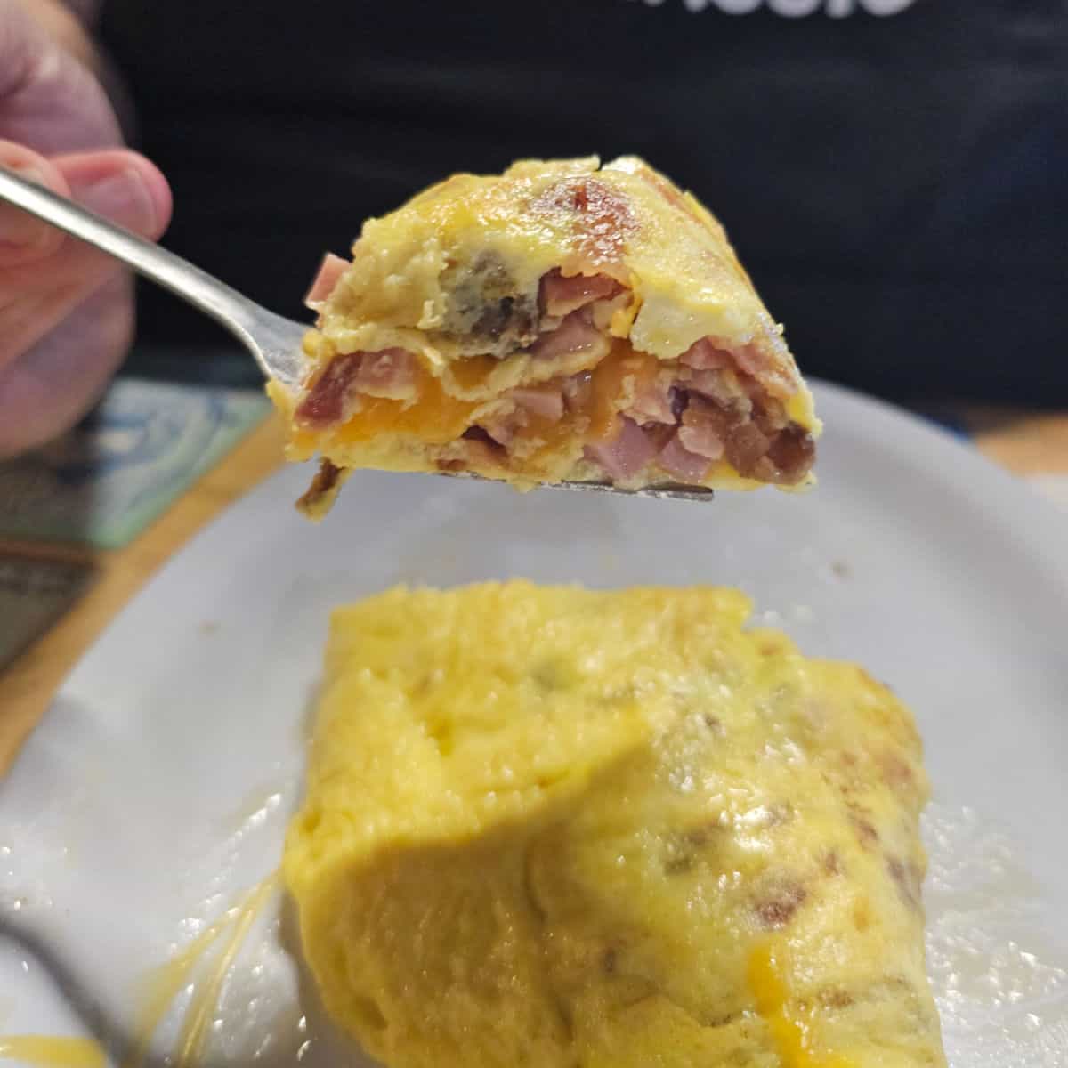 hand holding a fork with a large bite of meat filled omelet