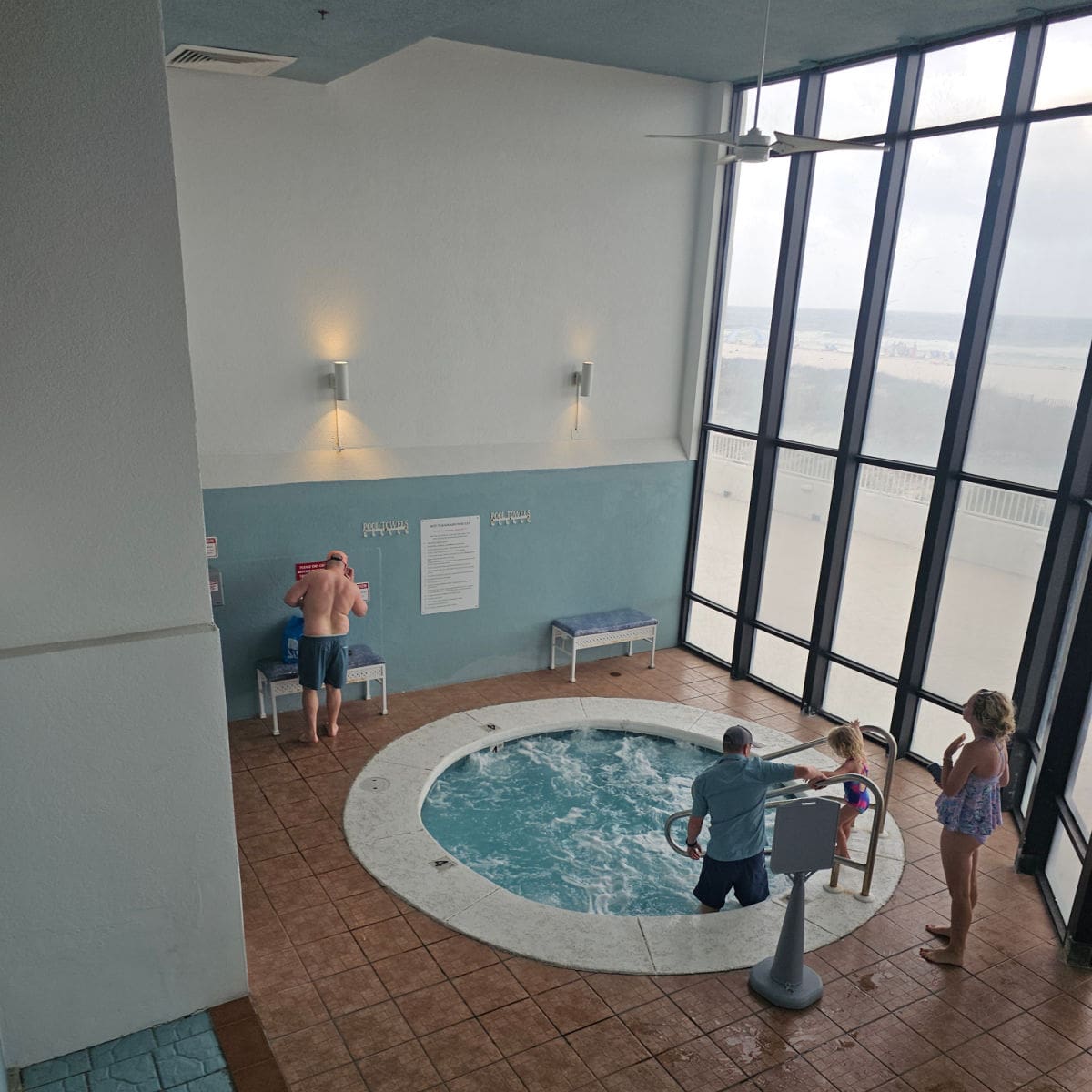 looking over a hote tub with two people getting into it, large windows looking out towards the beach