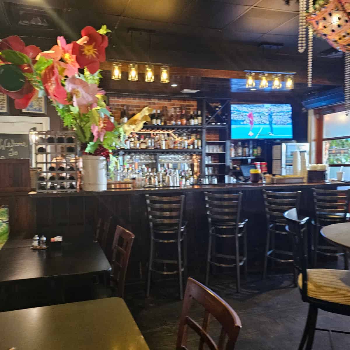 bar area with tall chairs along the bar, bottles on the bar, and tables and chairs under a floral display