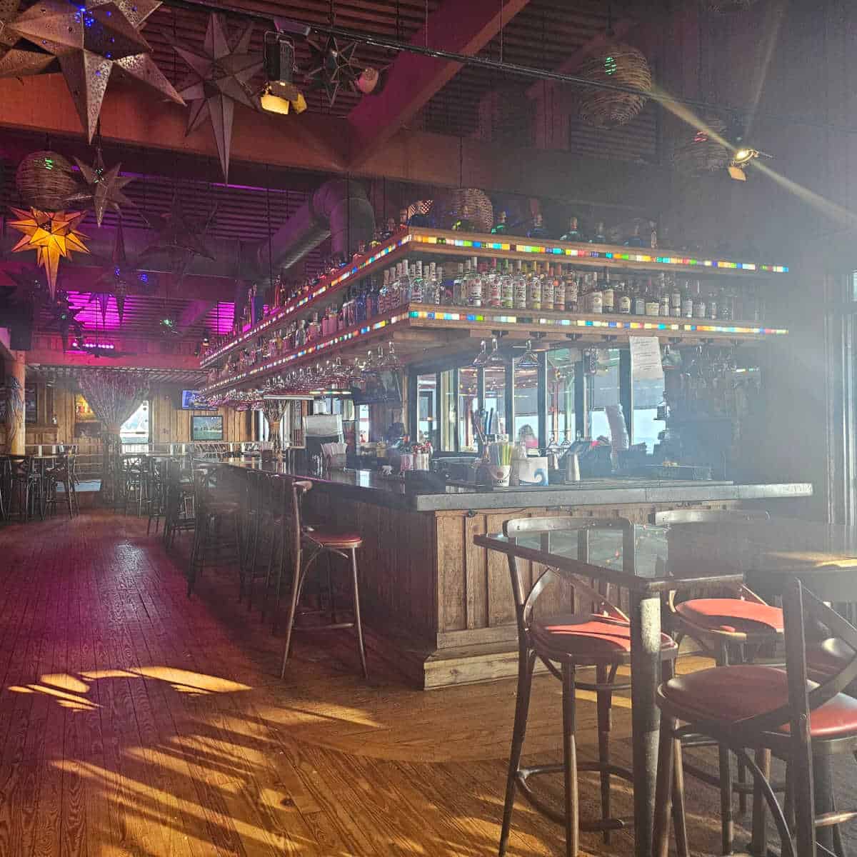 bar area with rows of bottles on the top, tall chairs pulled up to the bar, star lights hanging from the ceiling
