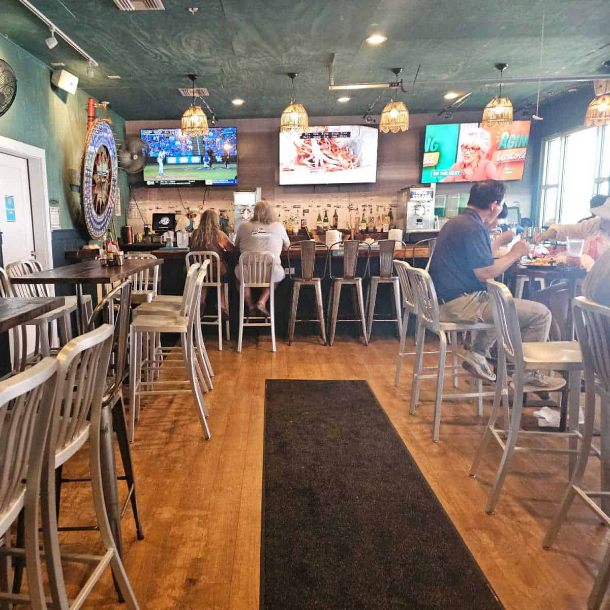 indoor bar with people in metal tall chairs along with tables with tall stools an chairs