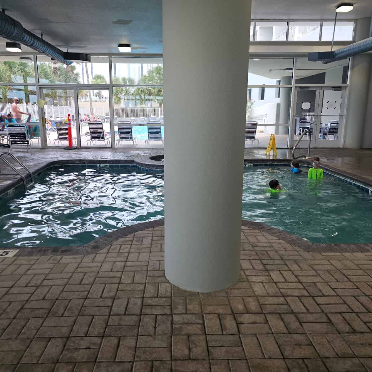 indoor pool with kids playing in the water looking out towards the outdoor pool area