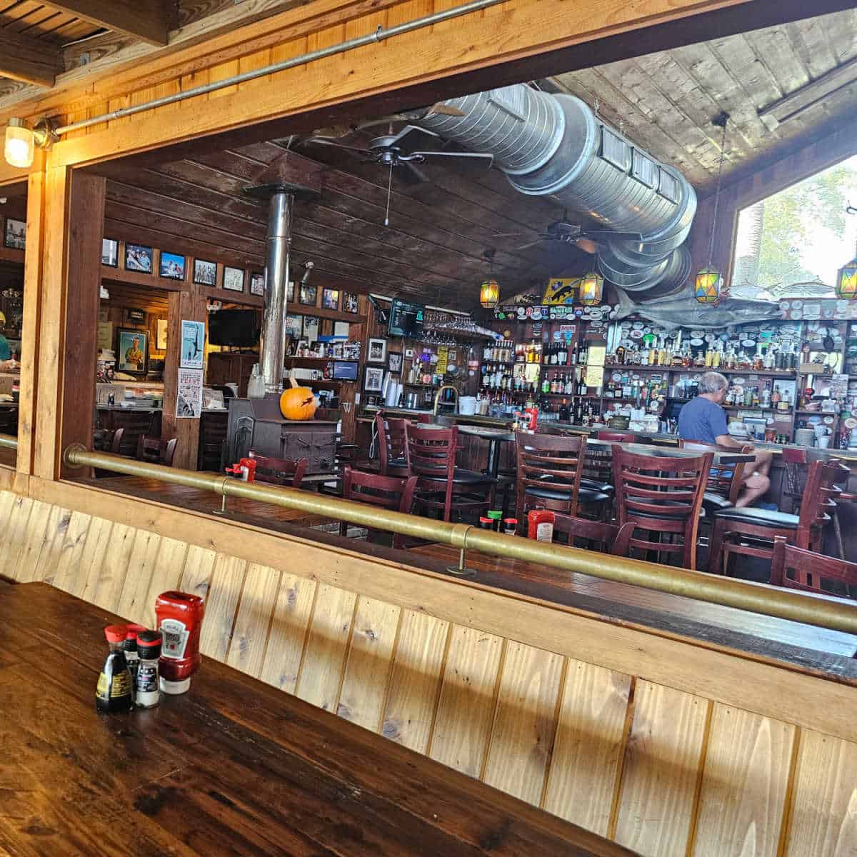 indoor bar with shelves of bottles, tall tables and chairs with a person sitting at the bar