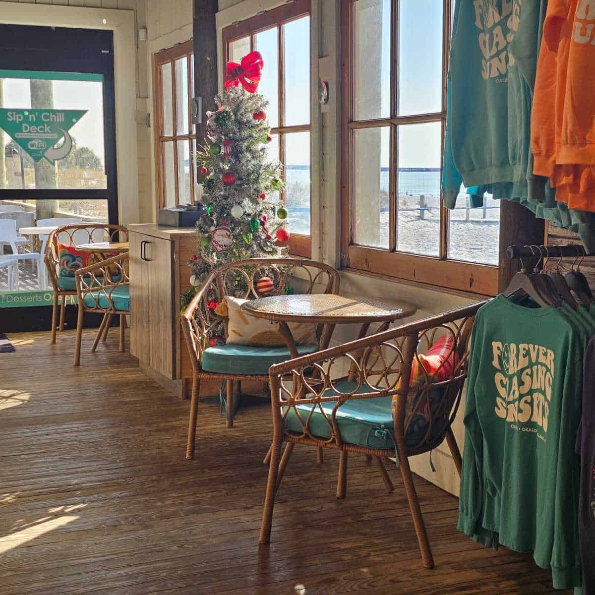table and chairs near a christmas tree, shirt that says forever chasing sunsets hanging on the wall