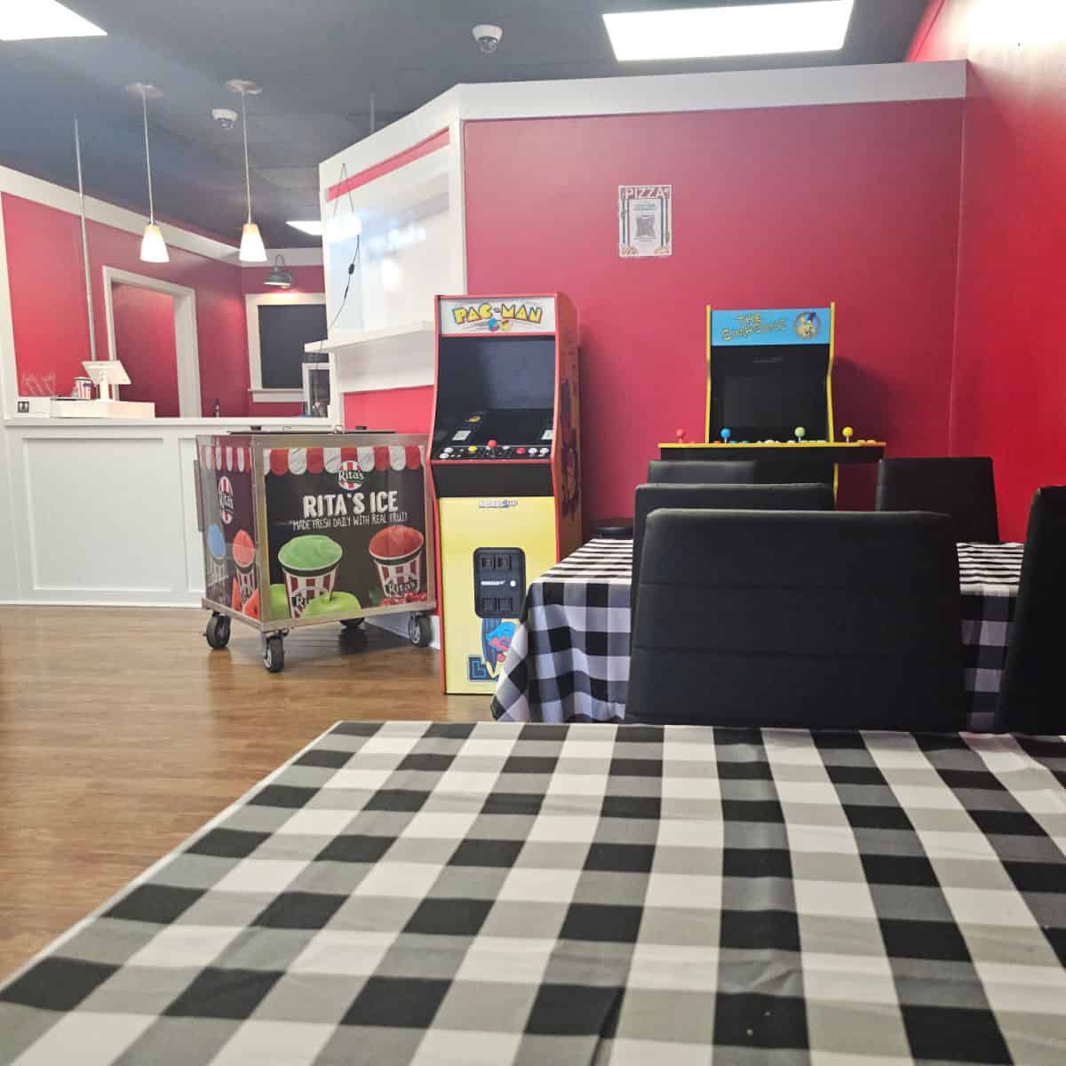 inside a restaurant with arcade games, black and white checkered tables, and bright red walls